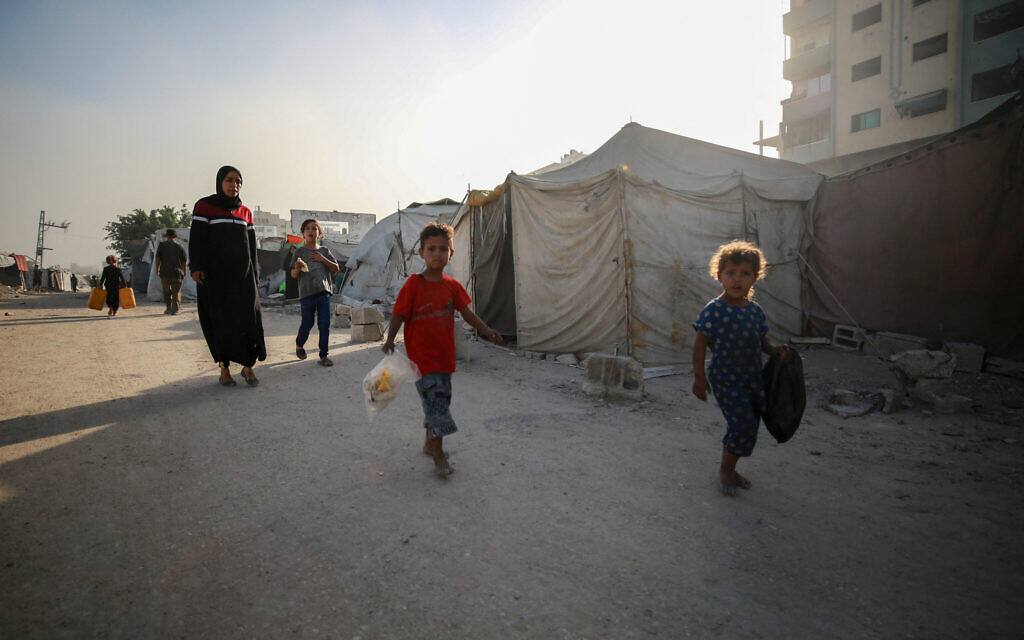 A Palestinian woman and children walk past a tent in Gaza City on August 29, 2025. (Photo by Bashar TALEB / AFP)