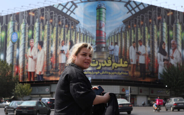 An Iranian woman walk past a billboard displaying pictures of nuclear scientists, centrifuges and a sentence reading in Farsi: " Science is the power", at the Enqelab square in Tehran, on August 29, 2025. (Photo by AFP)