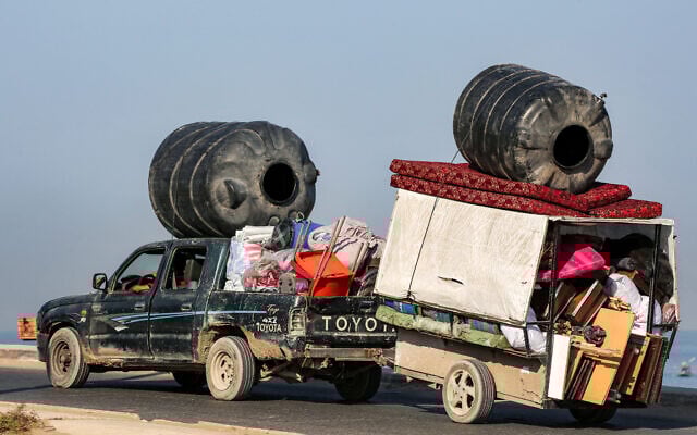 A vehicle towing a cart, both carrying cisterns and other belongings of displaced Palestinians fleeing south, moves along the coastal road through  Nuseirat in the central Gaza Strip on August 30, 2025.  (Photo by Eyad BABA / AFP)