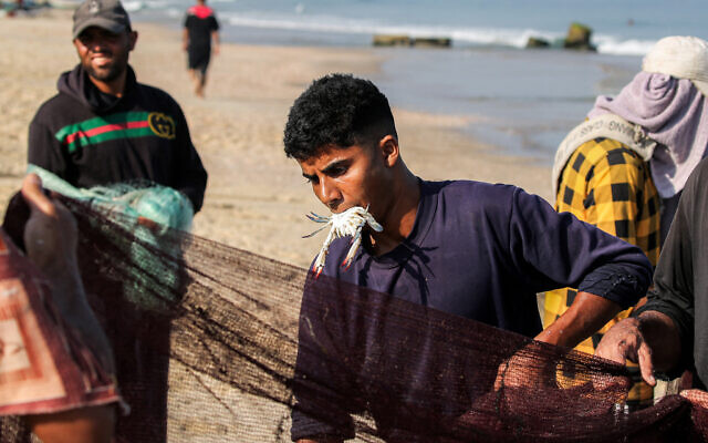 A fisherman holds a crab in his mouth as he pulls in a net to shore along a beach in the Nuseirat in the central Gaza Strip on August 30, 2025. (Photo by Eyad BABA / AFP)