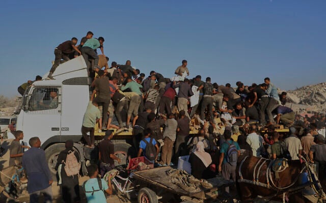 Palestinians get food and humanitarian aid from the back of a truck as it moves along the Morag corridor near Rafah, in the southern Gaza Strip, Monday, Aug. 4, 2025. (AP/Mariam Dagga)