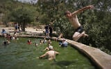 A man jumps in the water as people cool off in the Ein Lavan spring, amid a heat wave, in the outskirts of Jerusalem, August 13, 2025. (AP/Mahmoud Illean)