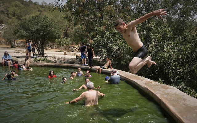 A man jumps in the water as people cool off in the Ein Lavan spring, amid a heat wave, in the outskirts of Jerusalem, August 13, 2025. (AP/Mahmoud Illean)