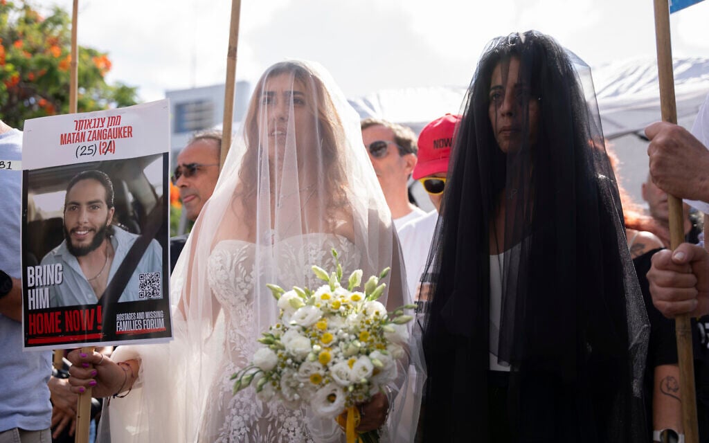 Holding a sign with a photo of her partner, Matan Zangauker, who is held hostage by Hamas, Ilana Gritzewsky, left, is accompanied by his mother, Einav Zangauker, as they arrive for a symbolic wedding ceremony at the plaza known as the hostages square in Tel Aviv, Israel, Sunday, Aug. 17, 2025, during a protest demanding a deal for the immediate release of all hostages (AP Photo/Maya Levin)