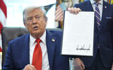 Illustrative: US President Donald Trump holds up a signed executive order requiring the Justice Department to investigate instances of flag burning, in the Oval Office of the White House, August 25, 2025. (AP Photo/Evan Vucci)