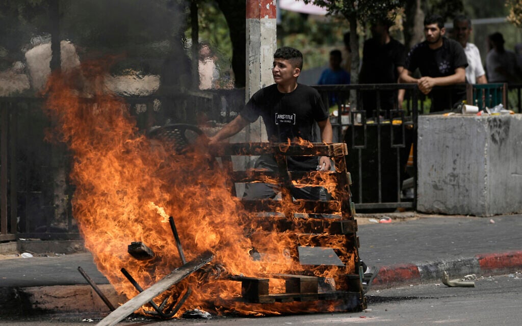 A Palestinian stands behind a barricade on fire during clashes with Israeli forces following a military raid in the West Bank city of Nablus, Wednesday, August 27, 2025. (AP Photo/Majdi Mohammed)