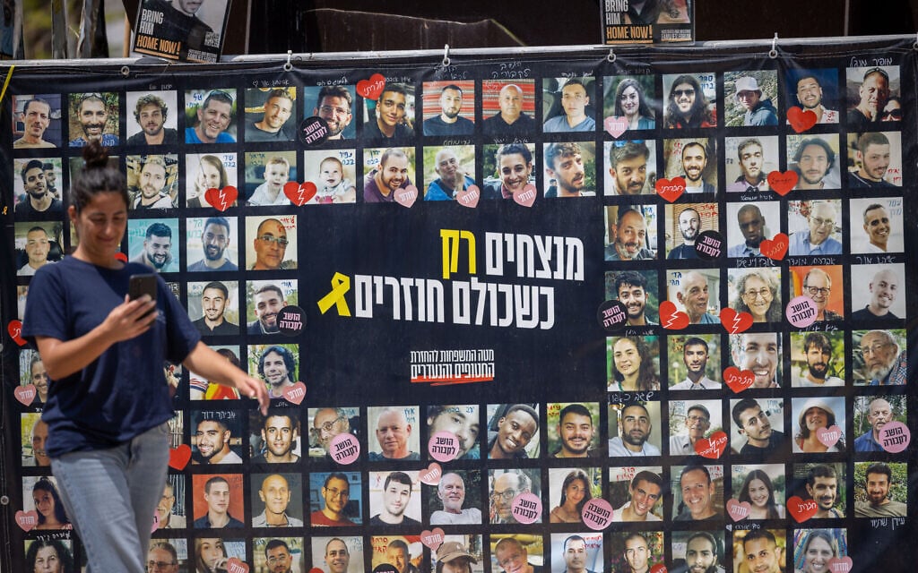 Visitors at Hostages Square in Tel Aviv walk past a banner with images of the captives on August 11, 2025. (Miriam Alster/ Flash90)