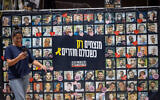 Visitors at Hostages Square in Tel Aviv walk past a banner with images of the captives on August 11, 2025. (Miriam Alster/ Flash90)