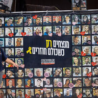 Visitors at Hostages Square in Tel Aviv walk past a banner with images of the captives on August 11, 2025. (Miriam Alster/ Flash90)