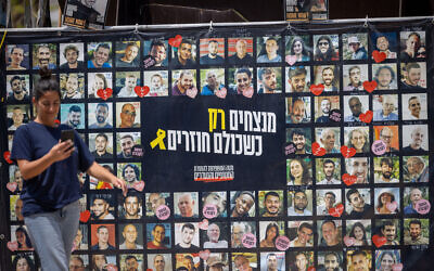 Visitors at Hostages Square in Tel Aviv walk past a banner with images of the captives on August 11, 2025. (Miriam Alster/ Flash90)
