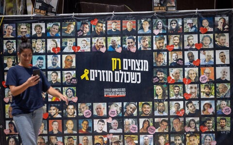 Visitors at Hostages Square in Tel Aviv walk past a banner with images of the captives on August 11, 2025. (Miriam Alster/ Flash90)