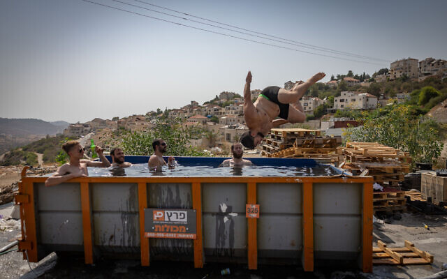 Jewish men swim in a garbage receptacle-turned-pool in the West Bank settlement of Beitar Illit on August 13, 2025. (Chaim Goldberg/Flash90)