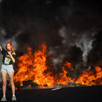 A protester blocks a main road near Lod as a fire blazes behind her, during a demonstration calling for the release of the hostages held by Hamas and a ceasefire in Gaza, August 26, 2025.  (Yonatan Sindel/Flash90)