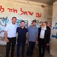 Finance Minister Bezalel Smotrich, second left, and Samaria Regional Council head Yossi Dagan, left, stand in a structure in the area of the former settlement of Sa-Nur in the northern West Bank, August 7, 2025. The two-word phrase, written in blue on the column on the photo's right, reads 'Death to Arabs.' (Roei Hadi/Samaria Regional Council)