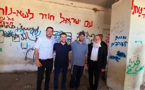 Finance Minister Bezalel Smotrich, second left, and Samaria Regional Council head Yossi Dagan, left, stand in a structure in the area of the former settlement of Sa-Nur in the northern West Bank, August 7, 2025. The two-word phrase, written in blue on the column on the photo's right, reads 'Death to Arabs.' (Roei Hadi/Samaria Regional Council)