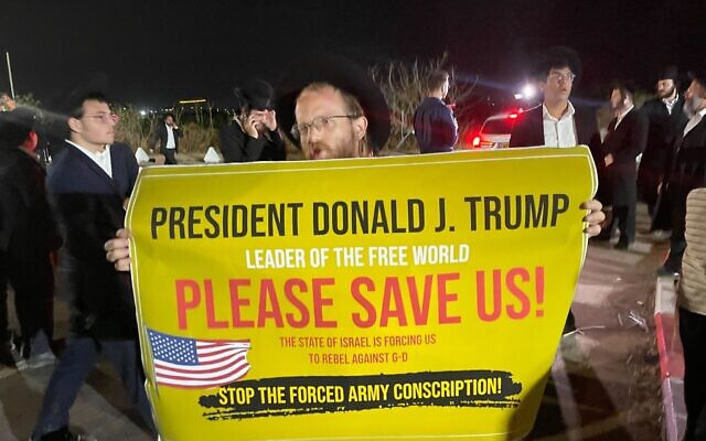 A member of the extremist ultra-Orthodox Jerusalem Faction holds up a sign calling on US President Trump to 'please save us,' at a rally against the arrest of draft-dodging yeshiva students outside of the military prison at Beit Lid, August 14, 2025. (Sam Sokol/Times of Israel)