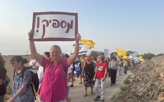 Alice Miller, who in the 1990s successfully sued the IDF for the right of women to enlist in the Israeli Air Force Flight Academy to become pilots, carries a placard saying 'Enough!' at a march close to the Gaza border, August 10, 2025.  (Naama Zevi Rivlin/ Pro-Democracy Protest Movement)