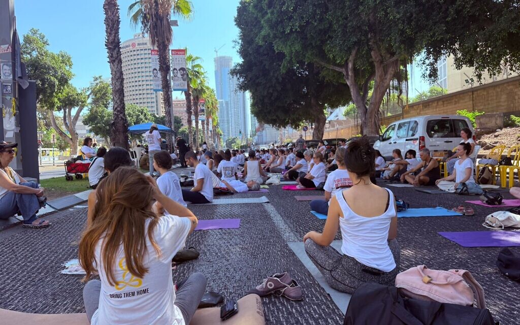 People take part in a yoga session as a form of peaceful protest outside the Defense Ministry headquarters in Tel Aviv on August 29, 2025, to mark a year since the murder of six hostages, including yoga instructor Carmel Gat, in Gaza. (Shani Tamim/Pro-Democracy Protest Movement)