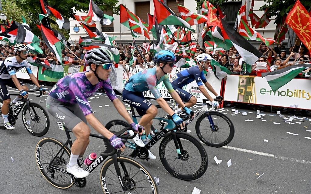 Cyclists compete as pro-Palestinian, anti-Israel protesters holding Palestinian and Basque flags demonstrate during the eleventh stage of the Vuelta a Espana cycling tour, a 167 km race from Bilbao to Bilbao, on September 3, 2025. (Photo by ANDER GILLENEA / AFP)