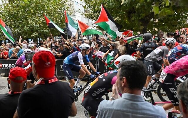 Team Israel Premier-Tech's Italian rider Marco Frigo (C) rides next to pro-Palestinian demonstrators at the start of the 12th stage of the Vuelta a Espana, a 144,9 km race between Laredo and Corrales de Buelna, on September 4, 2025. (ANDER GILLENEA / AFP)