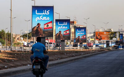 A man rides a scooter past signs depicting a Lebanese soldier saluting the national flag with the Arabic slogan 'We are all with you' along the highway leading to Beirut International Airport in southern Beirut on September 5, 2025. (ANWAR AMRO / AFP)