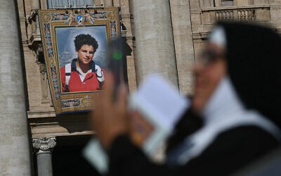 A nun checks her phone as a portrait of late Italian teenager Carlo Acutis is displayed onto the facade of Saint Peter's Basilica in the background ahead of a Holy Mass and canonization of Blessed Carlo Acutis and Pier Giorgio Frassati in St Peter's Square at the Vatican on September 7, 2025. (Filippo MONTEFORTE / AFP)