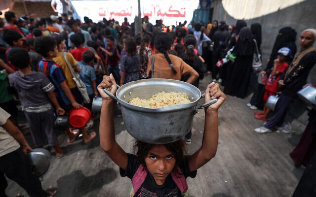 A Palestinian child walks away with a pot of rice obtained from a charity kitchen in the Nuseirat camp in the central Gaza Strip on September 14, 2025. (Photo by Eyad BABA / AFP)