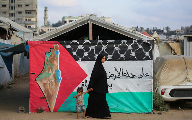 A Palestinian woman walks with a child past a Palestinian flag at the Bureij camp  in the central Gaza Strip on September 22, 2025. (Photo by Eyad BABA / AFP)