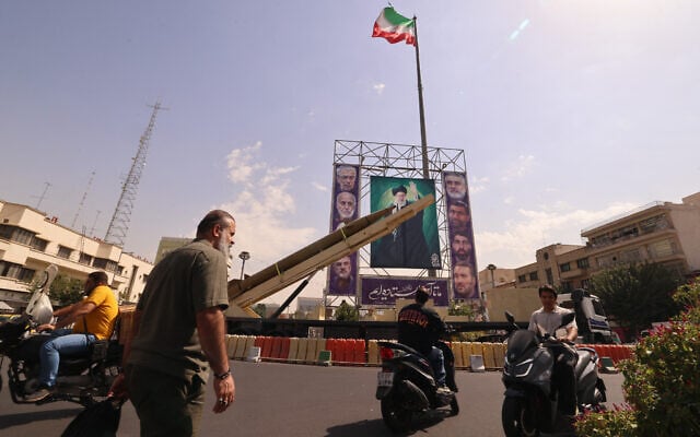 Iranians ride their motorcycles past a deactivated Kheibar Shekan ballistic missile in front of a picture of Iran's Supreme Leader Ayatollah Ali Khamenei in Tehran's Bahrestan Square on September 27, 2025, as part of an exhibit to mark the "Sacred Defense Week" commemorating the 1980-88 Iran-Iraq war. (Photo by ATTA KENARE / AFP)