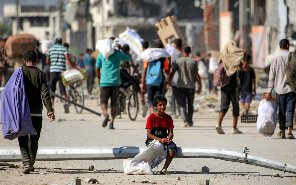 A boy sits on a toppled street light pole as around him people walk with humanitarian aid packages that they received from a distribution center run by the US and Israeli-backed Gaza Humanitarian Foundation in Nuseirat in the central Gaza Strip, on September 30, 2025. (Eyad BABA / AFP)