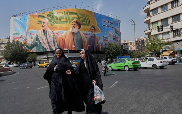 Two women walk past a huge banner showing the late commander of the Iran's Revolutionary Guard expeditionary Quds Force, Gen. Qassem Soleimani, who was killed in a US drone attack in 2020, and two late Hezbollah leaders Hassan Nasrallah, center, and Hashem Safieddine, who were killed in Israeli airstrikes in 2024, at the Enqelab-e-Eslami (Islamic Revolution) square, in Tehran, Iran, September 27, 2025. (AP Photo/Vahid Salemi)