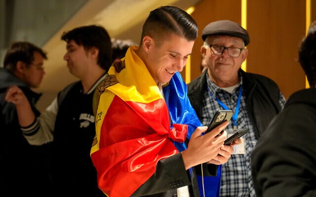 A supporter of the pro-EU Party of Action and Solidarity (PAS) draped in the Moldovan flag smiles as he checks partial results on a phone after the polls closed for the parliamentary election, in Chisinau, Moldova, Sunday, Sept. 28, 2025. (AP Photo/Vadim Ghirda)