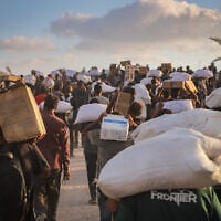 Displaced Palestinians carry food parcels and supplies from aid trucks near the Zikim border crossing between Israel and Beit Lahiya, in the northern Gaza Strip, August 18, 2025. (Khalil Kahlout/ Flash90)