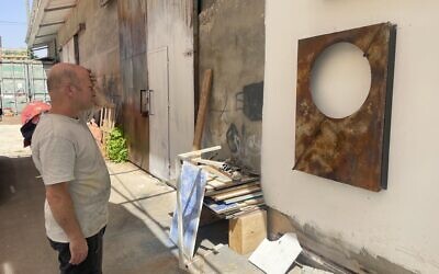 Artist Avinadav Begin stands outside his Even Sapir workshop on September 21, 2025, contemplating a work in progress (Jessica Steinberg/Times of Israel)
