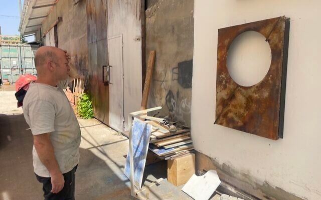 Artist Avinadav Begin stands outside his Even Sapir workshop on September 21, 2025, contemplating a work in progress (Jessica Steinberg/Times of Israel)