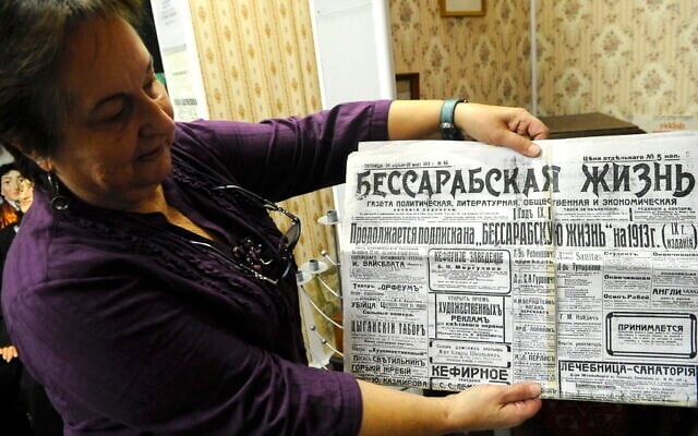 Librarian Olga Sivak holds up a newspaper from 1913, Bessarabian Life, at the Jewish Museum of Moldova in Chișinău. (Photo by Larry Luxner via JTA)