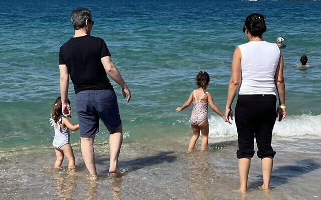 Omri Miran pictured at the beach with his wife Lishay and two daughters on October 17, 2025, soon after his discharge from the hospital, and four days after he was released from more than two years in Hamas captivity in Gaza. (Screenshot via X; Eli Teichman and Shir Katz)