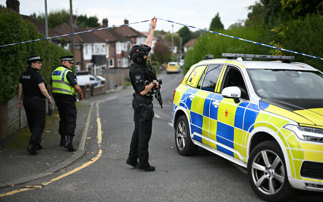 An armed police officer lifts a cordon for a police car to be driven away from White House Avenue, near to the Heaton Park Hebrew Congregation synagogue in Crumpsall, north Manchester, on October 2, 2025 (Oli SCARFF / AFP) An armed police officer lifts a cordon for a police car to be driven away from White House Avenue, near to the Heaton Park Hebrew Congregation synagogue in Crumpsall, north Manchester, on October 2, 2025 (Oli SCARFF / AFP)