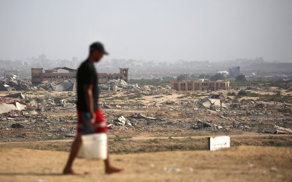 A Palestinian man transports buckets of water next to a coastal path northwest of Nuseirat refugee camp, in the Gaza Strip, October 4, 2025. (Eyad BABA / AFP)
