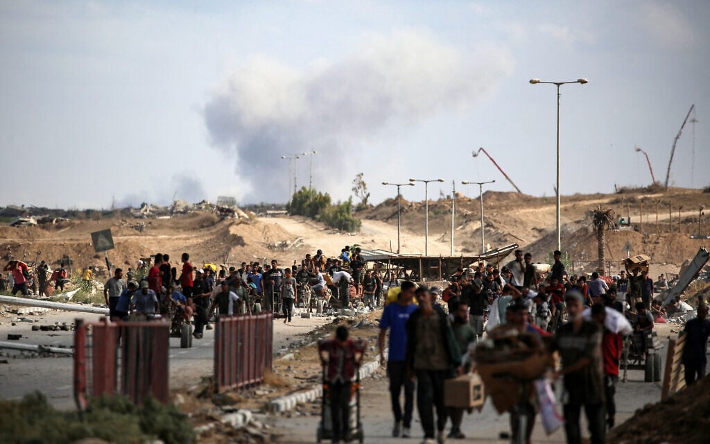 A plume of smoke rises in the background as Palestinians return from a food distribution point run by the US and Israeli-backed Gaza Humanitarian Foundation, near the Netzarim Corridor in the central Gaza Strip on October 5, 2025. (Eyad BABA / AFP)