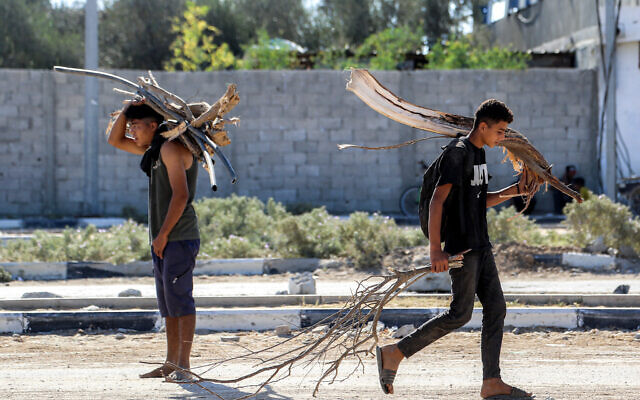 Boys walk with collected tree branches and pipes that will be used as firewood, at a camp for people displaced by war in northern Nuseirat, in the central Gaza Strip on October 7, 2025. (BASHAR TALEB / AFP)