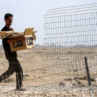 A man walks with a cardboard box bearing the Gaza Humanitarian Foundation (GHF) logo and loaded with pieces of wood as he walks near Nuseirat in the central Gaza Strip on October 10, 2025. (Eyad BABA / AFP)