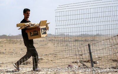 A man carries a cardboard box bearing the Gaza Humanitarian Foundation (GHF) logo and loaded with pieces of wood, as he walks near Nuseirat in the central Gaza Strip, on October 10, 2025. (Eyad BABA / AFP)