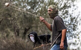 A masked Jewish extremist swings a slingshot while hurling stones at Palestinians who had gathered for the annual olive harvest season, during an attack by Israeli settlers on the Palestinian village of Beita, south of Nablus in the West Bank, on October 10, 2025. (Jaafar ASHTIYEH / AFP)