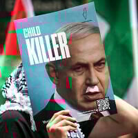 A demonstrator holds a placard showing Prime Minister Benjamin Netanyahu with a Hitler-style mustache and text that reads "child killer," during a rally in Sydney on October 12, 2025. (David Gray/ AFP)