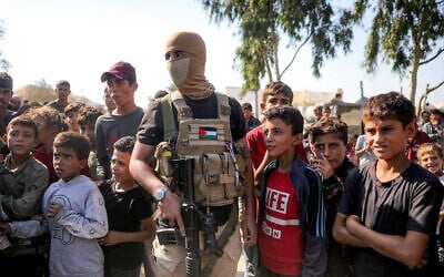 A masked member of the Hamas military wing stands guard next to children in the south of Deir el-Balah in the central Gaza Strip on October 13, 2025. (Bashar TALEB / AFP)
