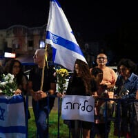 People carry flowers and Israeli flags upon the arrival of vehicles transporting the bodies of four hostages, in front of the National Center for Forensic Medicine in Tel Aviv on October 13, 2025. The Hebrew sign reads, "Sorry." (Jalaa MAREY / AFP)