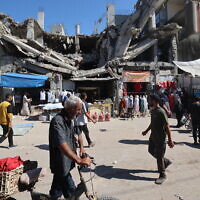 Palestinians walk past a destroyed building at a makeshift market in the Nuseirat refugee camp, located in the central Gaza Strip, on October 15, 2025. (Eyad BABA / AFP)