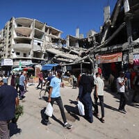 Palestinians walk past a destroyed building at a makeshift market in the Nuseirat refugee camp, located in the central Gaza Strip, on October 15, 2025. (Eyad BABA / AFP)