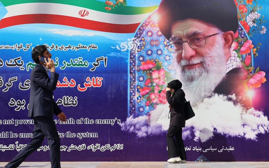 Iranians walk past a poster featuring Iran's Supreme Leader Ayatollah Ali Khamenei outside the venue of the 22nd Police and Security Equipment Exhibition at Imam Khomeini Mosque in Tehran on October 15, 2025. (Photo by ATTA KENARE / AFP)